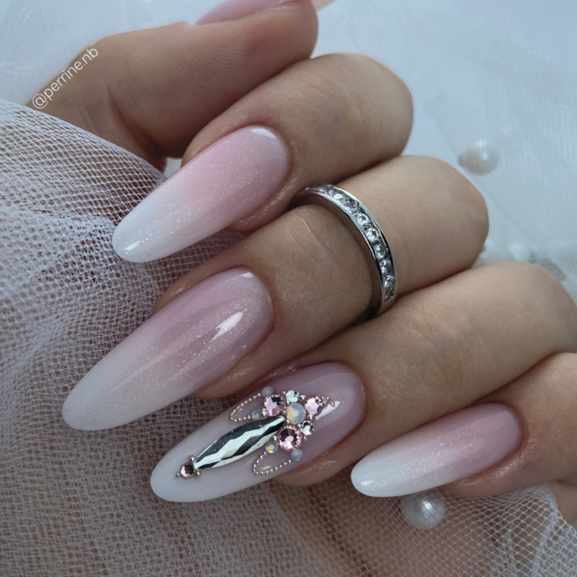 Pose gel forme amande rose pâle avec dégradé blanc et décoration strass délicate sur ongle accent.